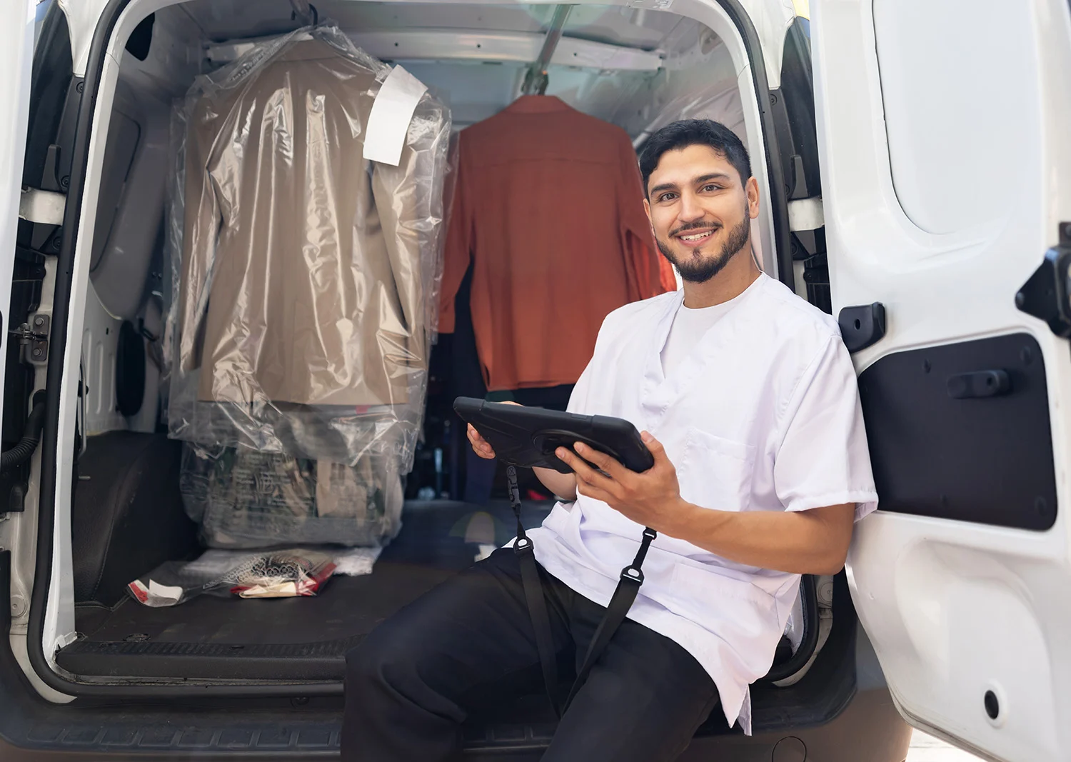 man in the back of dry cleaner workvan filled with hanging clothing